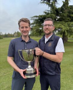 A photo showing 2026 Suffolk Amateur Foursomes Champions Daniel Hedges and Russel Oakey holding the winning cup on a golf course.